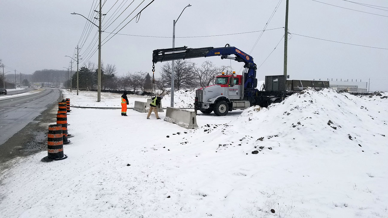 Crane Truck placing concrete barriers on a snowy road